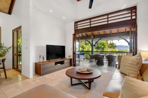 a living room with a couch and a tv and a table at Monsoon Villa A - Central Balinese-style Pool Oasis in Port Douglas