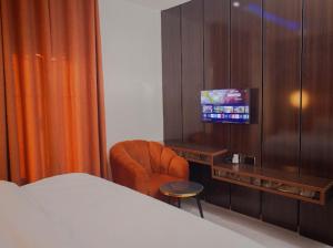 a bedroom with a bed and a chair and a television at Maxbliss Optimum Royal Hotel in Benin City