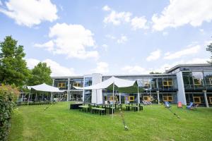 a building with tables and white umbrellas in a field at GenoHotel Baunatal in Baunatal