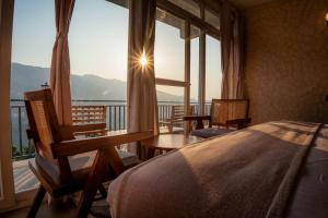 a bedroom with a bed and chairs and a large window at Enchanted Hills Farmstay in Mukteshwar