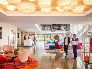 two people walking through a lobby with red chairs at Cabot Hotel Bordeaux - MGallery Collection in Le Pian-Médoc +106 photos