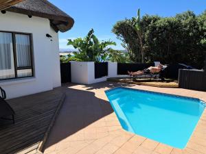 a swimming pool next to a house with a person sitting in a chair at i-LOLLO Bed & Breakfast at the River Mouth in St Francis Bay