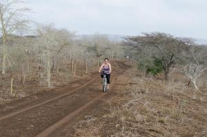 a woman riding a bike on a dirt road at Umziki Chalets in Mkuze