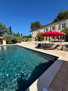 a swimming pool with a red umbrella and a building at Appel du Luberon in Mérindol