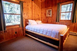 a bed in a wooden room with two windows at Spacious Rustic Cabin with Vaulted Ceilings, Full Kitchen, Fireplace & Large Deck Near Babbitt, Minnesota in Babbitt