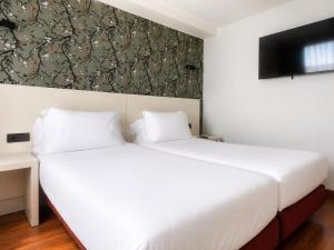 a bedroom with two beds and a tv on the wall at Hotel Apartamentos San Fermín Pamplona in Pamplona