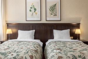 two beds in a hotel room with paintings on the wall at Gertrude Hotel self check-in in Riga