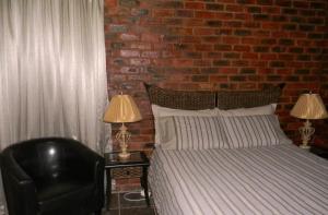 a bedroom with a bed and a black chair and two lamps at La Postma House in Postmasburg