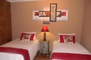 two beds in a room with a lamp on a table at La Postma House in Postmasburg