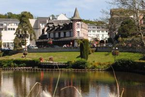 a building with a tower next to a body of water at La Potinière Du Lac Appartements in Bagnoles de l'Orne