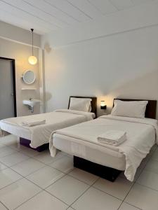 two beds in a room with white walls at The Northeast Hotel in Si Sa Ket