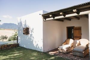 a white house with two chairs on a patio at Vineyard Cottage at Bosman Wines in Wellington