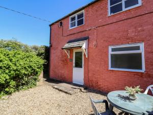 a red brick building with a white door and a table at Walk Farm Cottage in Gloucester