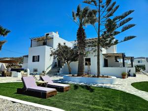 a white house with two chairs and palm trees at Coralli Beach Apartments in Mikri Vigla