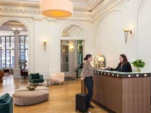 a woman standing at a reception desk in a lobby at Mercure Lille Roubaix Grand Hôtel in Roubaix