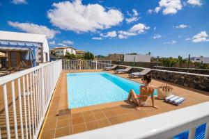 a woman sitting on the edge of a balcony with a swimming pool at Villas & Apartamentos Tao Mazo in Lajares