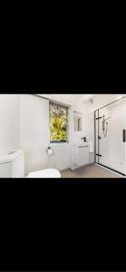 a white bathroom with a sink and a window at Sunbird House Piha in Piha +10 photos