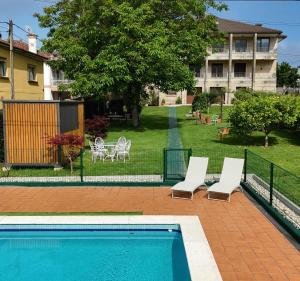 a swimming pool with two white chairs and a house at Apartamentos Ria de Aldan in Aldán