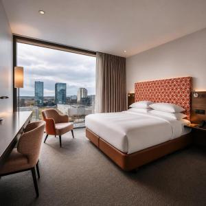 a hotel room with a bed and a desk and a large window at Windmill Frankfurt Niederrad in Frankfurt