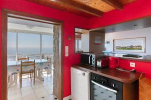 a kitchen with red walls and a view of the ocean at Villa Timao Plage in Batz-sur-Mer