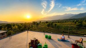 a woman sitting on a roof watching the sunset at Aahista Stays- Mountain view homestay in Bīr