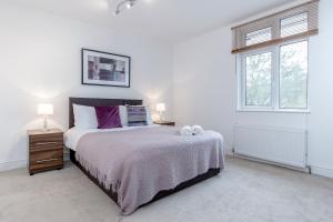 a white bedroom with a large bed with purple pillows at Royal Apartments - Heathrow in Hillingdon