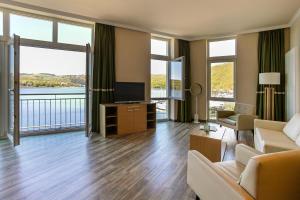 a living room with a television and large windows at Dormio Hotel Der Seehof in Heimbach