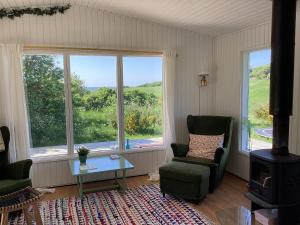 a living room with a chair and a table and two windows at Peaceful Cottage By The Beach And Nature in Spottrup