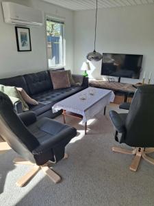a living room with a black couch and two chairs at Lovely Cottage Full Of Holiday Atmosphere in Rødby