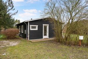 a small black house with a porch in a yard at Beautiful Holiday Home On An Undisturbed Plot in Rødby