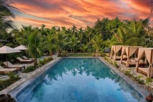 a pool at a resort with chairs and palm trees at Hidden Valley Eco Retreat Trang An in Ninh Binh