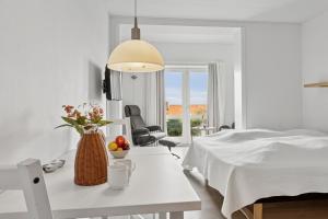a white bedroom with a bed and a table with flowers at Pension Koch Apartment 6 in Gudhjem