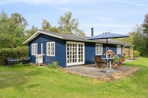 a blue cottage with a table and an umbrella at Renovated Classic Cottage Close To Beach in Roslev