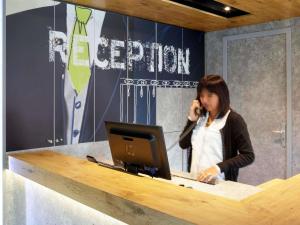 a woman talking on a cell phone at a desk with a computer at ibis budget Pontarlier in Pontarlier
