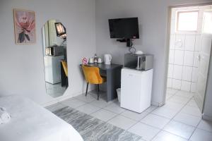 a room with a desk with a television and a kitchen at Divine Guest Lodge in Rustenburg