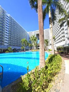 a large swimming pool with palm trees and buildings at Shell Residences Staycation MOA & NAIA by Keith in Manila