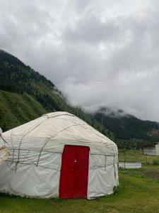 a white tent with a red door in a field at Murat Lyazzat Hotel in Kurmenty