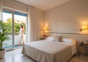 a hotel room with a bed and a woman walking on a balcony at Eden Torre Canne in Torre Canne