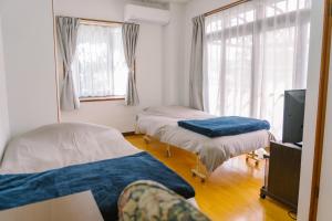 a room with two beds and a tv and windows at 温泉街近くの一棟貸し ひだまり in Kirishima