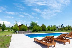 a swimming pool with two wooden chairs next to it at Finca La Vilina - Cabaña Aurora in San Rafael