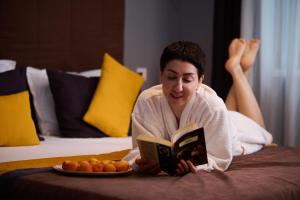 a woman laying on a bed reading a book with a plate of food at REGINA Bed&Wine in Varna City