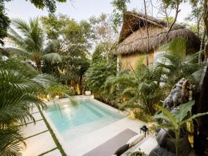 a swimming pool in a garden with a thatch roof at Ikal Bungalows Tulum in Tulum