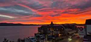 a sunset over a city with a building and the water at Del Lago Sky Hotel in San Carlos de Bariloche