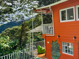 a red house with a green chair on a deck at Nan La Tigra in El Rosario