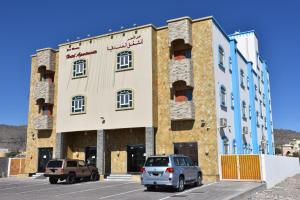 un bâtiment avec deux voitures garées dans un parking dans l'établissement Green Mountain Hotel Apartments, à Al ‘Aqar