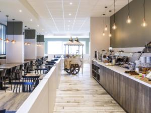 a restaurant with a long counter with tables and chairs at ibis Styles Nieuwpoort in Nieuwpoort