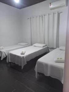 two beds in a room with white walls at Hotel Vale do Sol in Votuporanga