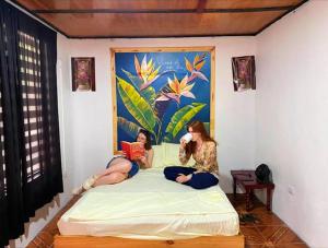 two women sitting on a bed reading books at Blackout Party Hostel and Experiences in Fortuna