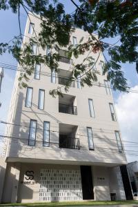 a tall white building with windows and a tree at Student Site - Coliving Hotel in Montería