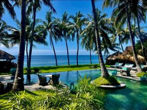 a resort pool with palm trees and the ocean at Louka Beach Bali in Tianyar